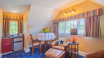 A room with a dining table, chairs, a small side table with a lamp, a decorative pillow, and a window with curtains.