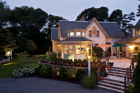 A two-story house with a well-lit front porch, a staircase leading to the entrance, and a garden with various plants and flowers.