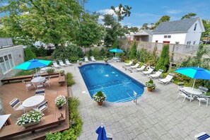 A rectangular swimming pool with lounge chairs and umbrellas, surrounded by a wooden deck and potted plants. - Winstead Inn (Harwich)
