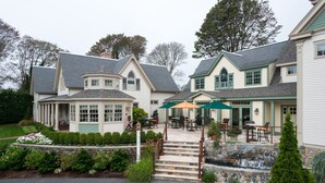 A large, two-story house with a covered patio area, outdoor seating, and a stone waterfall feature. - Winstead Inn (Harwich)