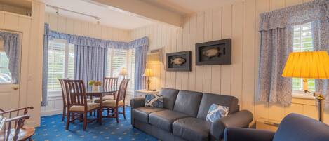 A room with a blue patterned carpet, a leather sofa, wooden chairs, a dining table, and framed fish pictures on the wall.