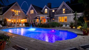 A large swimming pool with a fountain, surrounded by lounge chairs and umbrellas, set against a stone building with multiple windows and a balcony. - Winstead Inn (Harwich)
