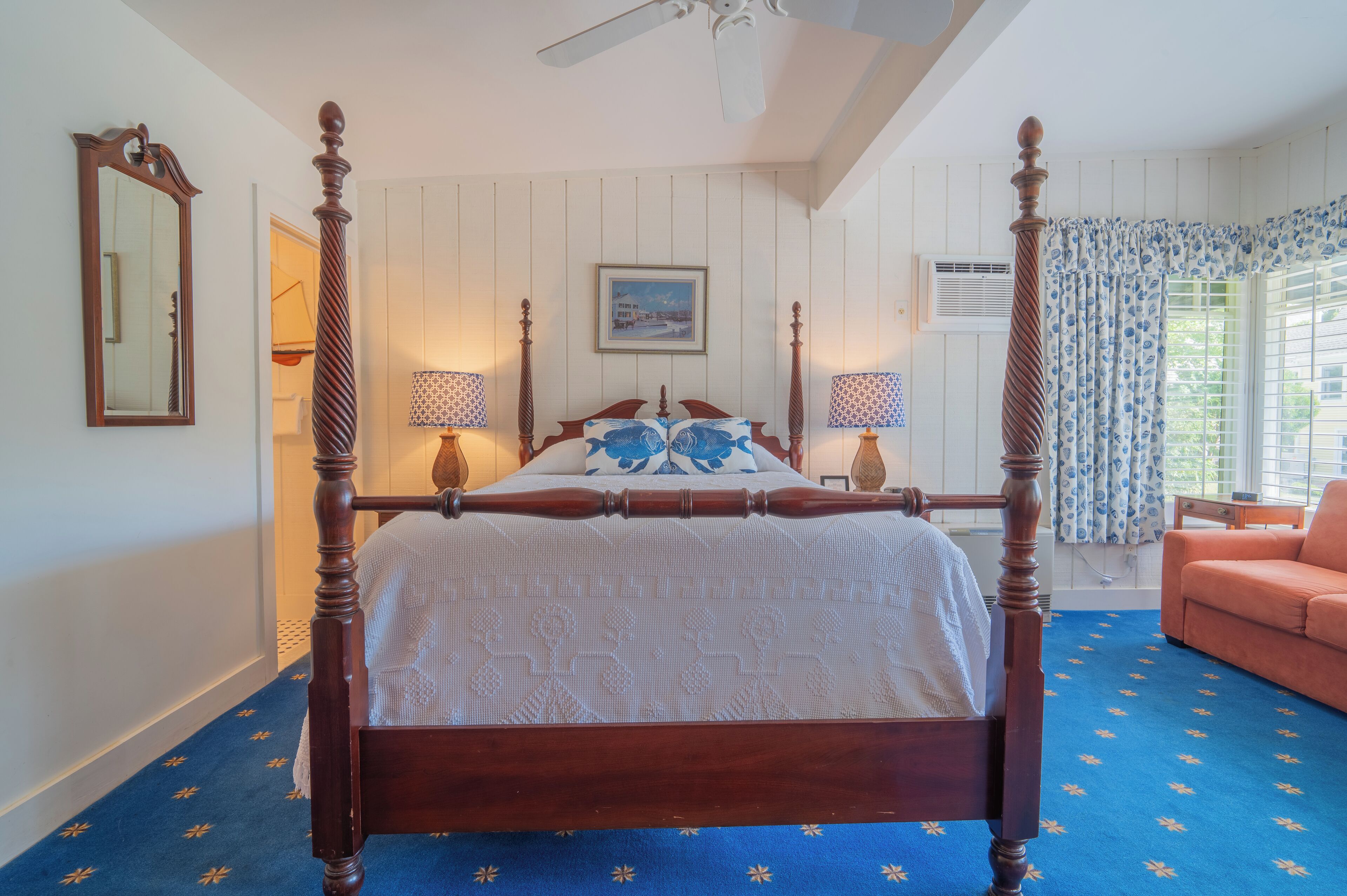 A four-poster bed with a white bedspread, two bedside lamps, and a framed picture on the wall.