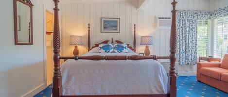 A four-poster bed with a white bedspread, two bedside lamps, and a framed picture on the wall.