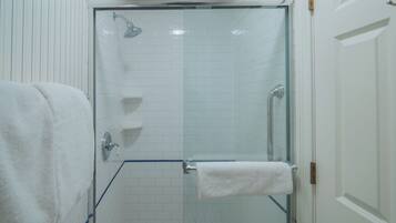 Ducha con cerramiento de vidrio, pared con azulejos blancos, una toalla blanca en la pared y una puerta blanca.