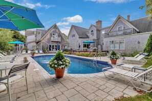 A swimming pool with lounge chairs and umbrellas, surrounded by stone buildings with a patio area. - Winstead Inn (Harwich)