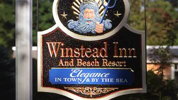 Placa do Winstead Inn e Beach Resort, com um logotipo mostrando uma figura segurando um tridente e estrelas, e o texto: 'Elegância na cidade e à beira-mar'.