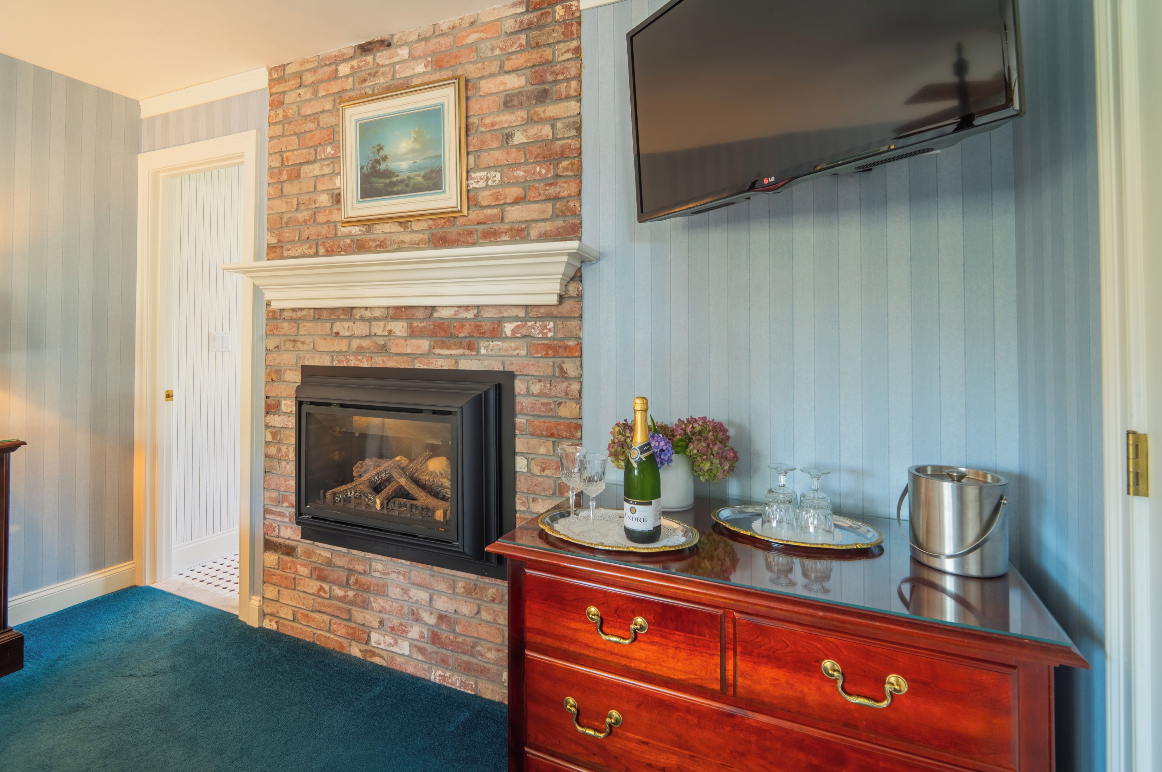 A room with a brick fireplace, a wooden dresser, and a mounted television.