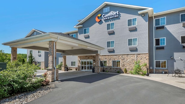 Un bâtiment de la chaîne Comfort Inn & Suites, doté d’une entrée abritée, de piliers en pierre et surplombé d’un ciel bleu clair.