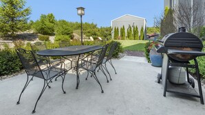 Une terrasse extérieure avec une table ronde et des chaises, un barbecue et un lampadaire.