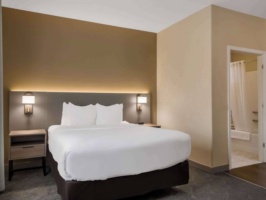 A hotel room with a large bed, bedside tables, and wall-mounted lamps.