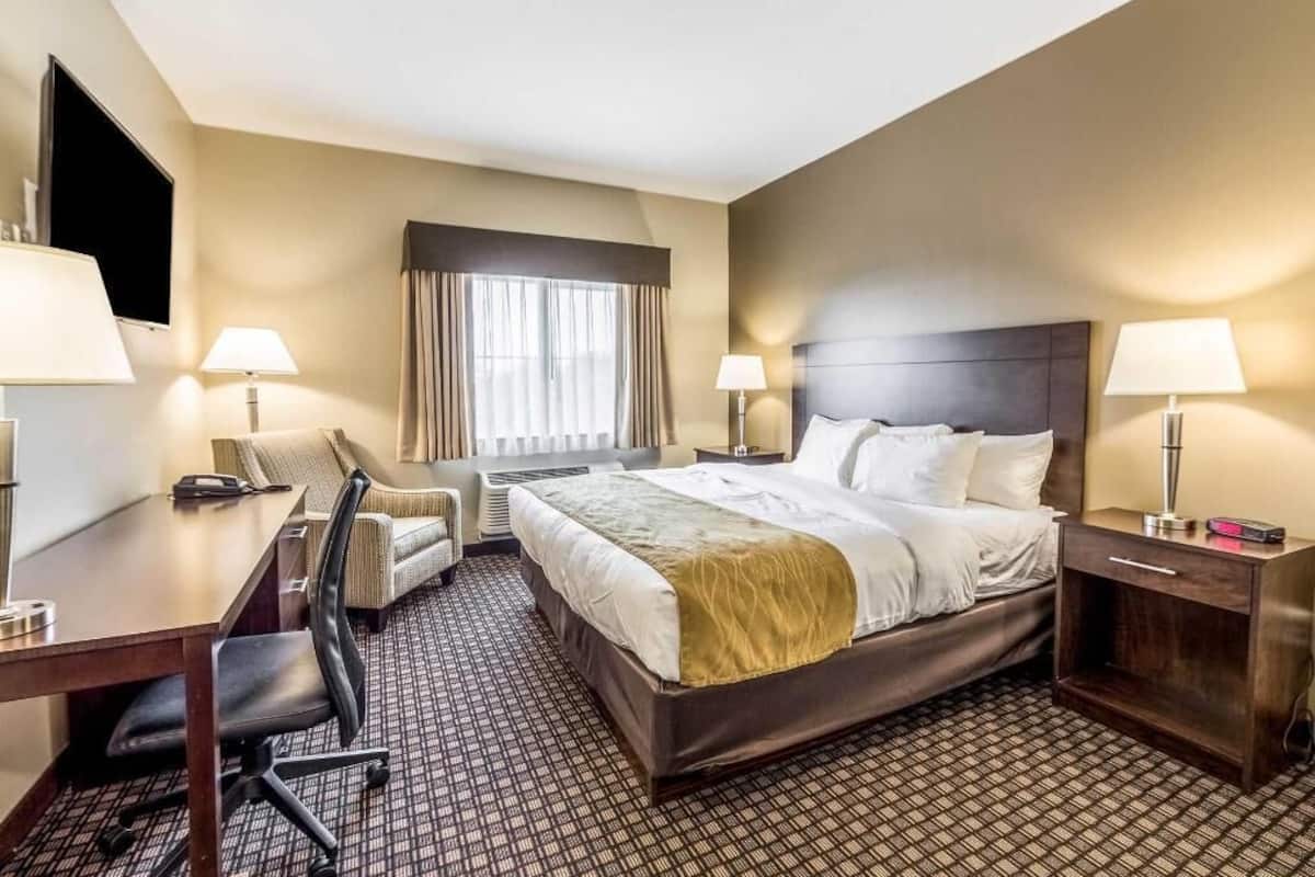 A hotel room with a bed, desk, chair, and a TV.
