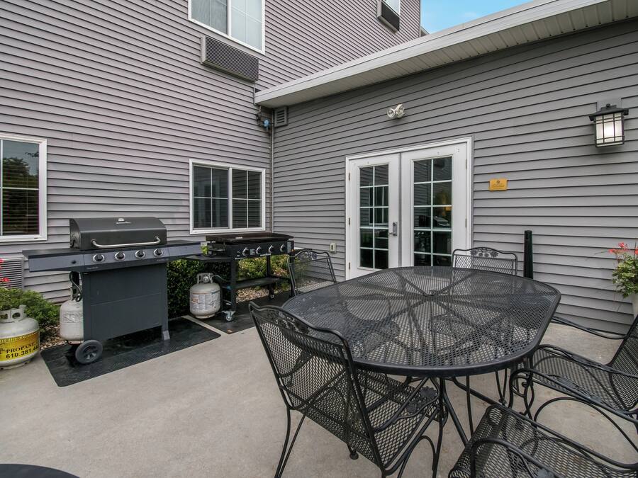 A patio with a grill, outdoor table, chairs, and potted plants.