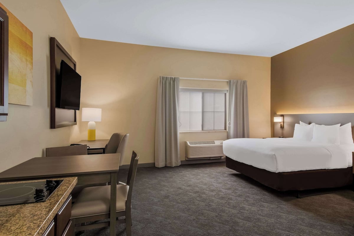 A hotel room with a bed, a desk, a chair, a TV, a window with curtains, and an air conditioning unit.