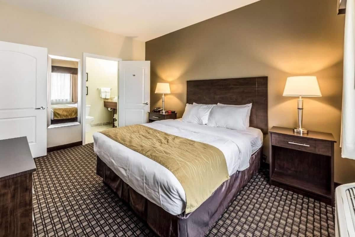 A hotel room with a large bed, bedside tables, a wardrobe, and a bathroom visible through an open door.