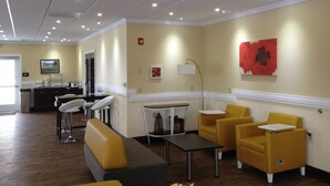 Un hall d’hôtel avec un comptoir d’accueil, un espace salon avec des chaises jaunes, un canapé gris et des œuvres d’art accrochées aux murs.