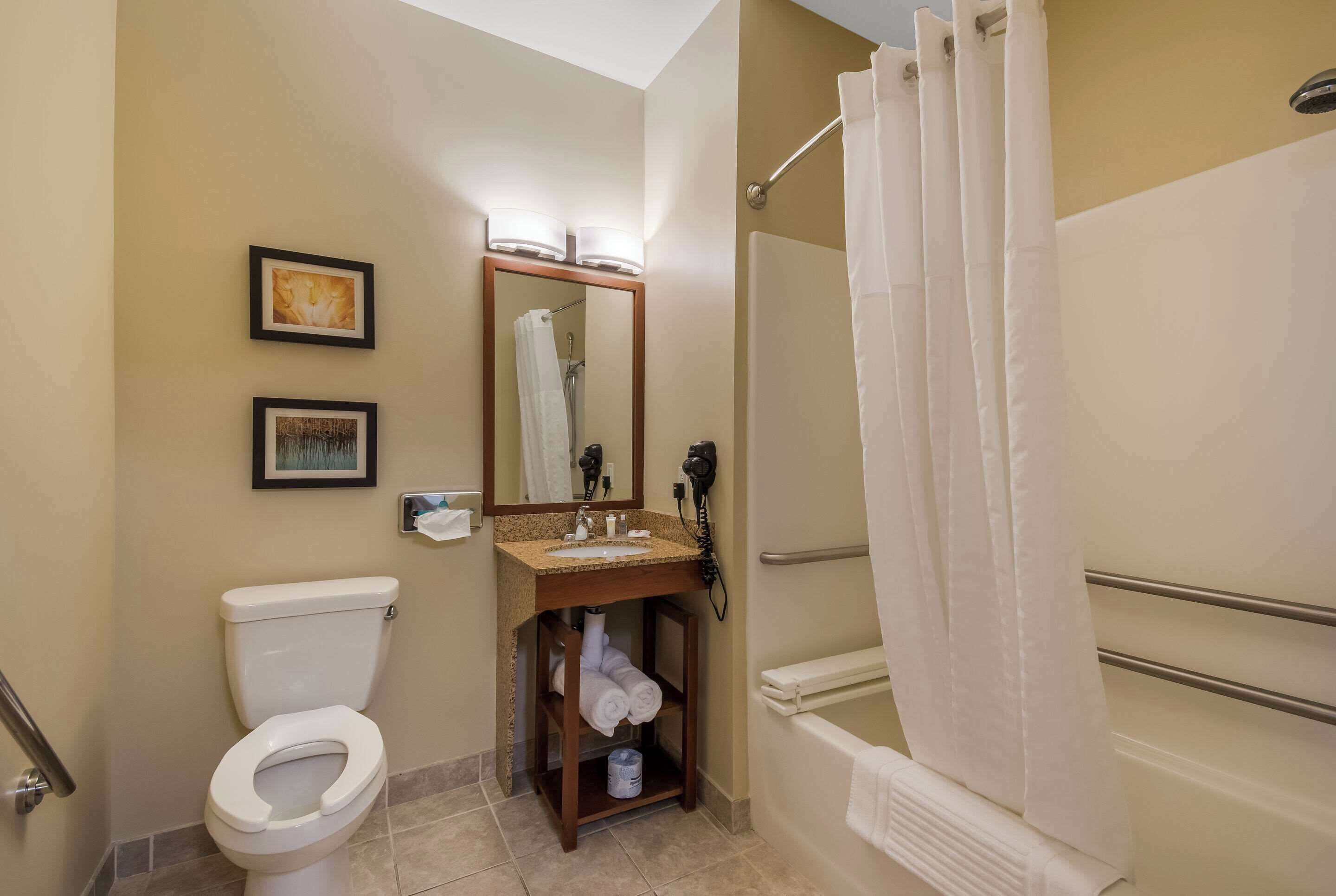 A bathroom with a toilet, sink, mirror, and shower area.