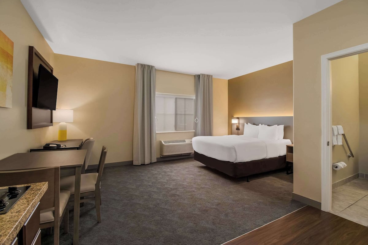 A hotel room with a bed, a desk with a chair, a TV mounted on the wall, and a window with curtains.