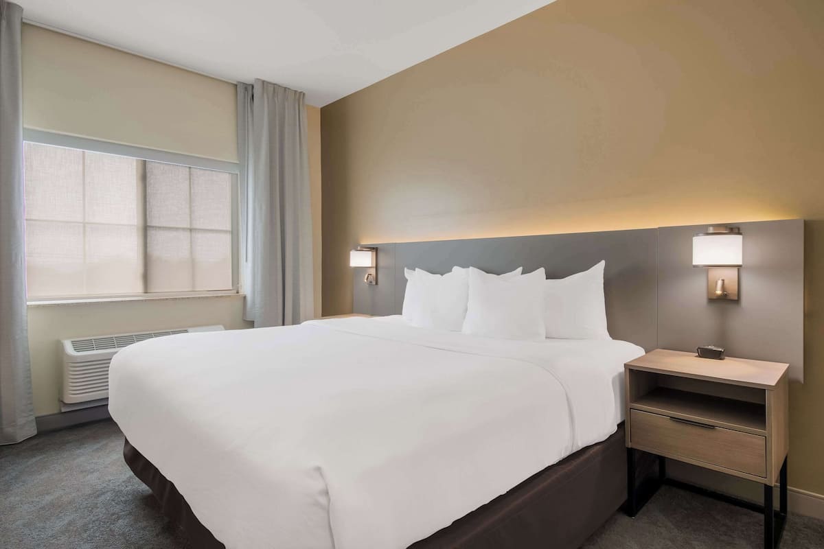 A hotel room with a large bed, bedside tables, and a window with curtains.