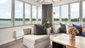 A modern room with a sofa, a table, and a view of a lake. - Zollenspieker Fährhaus (Hamburg)