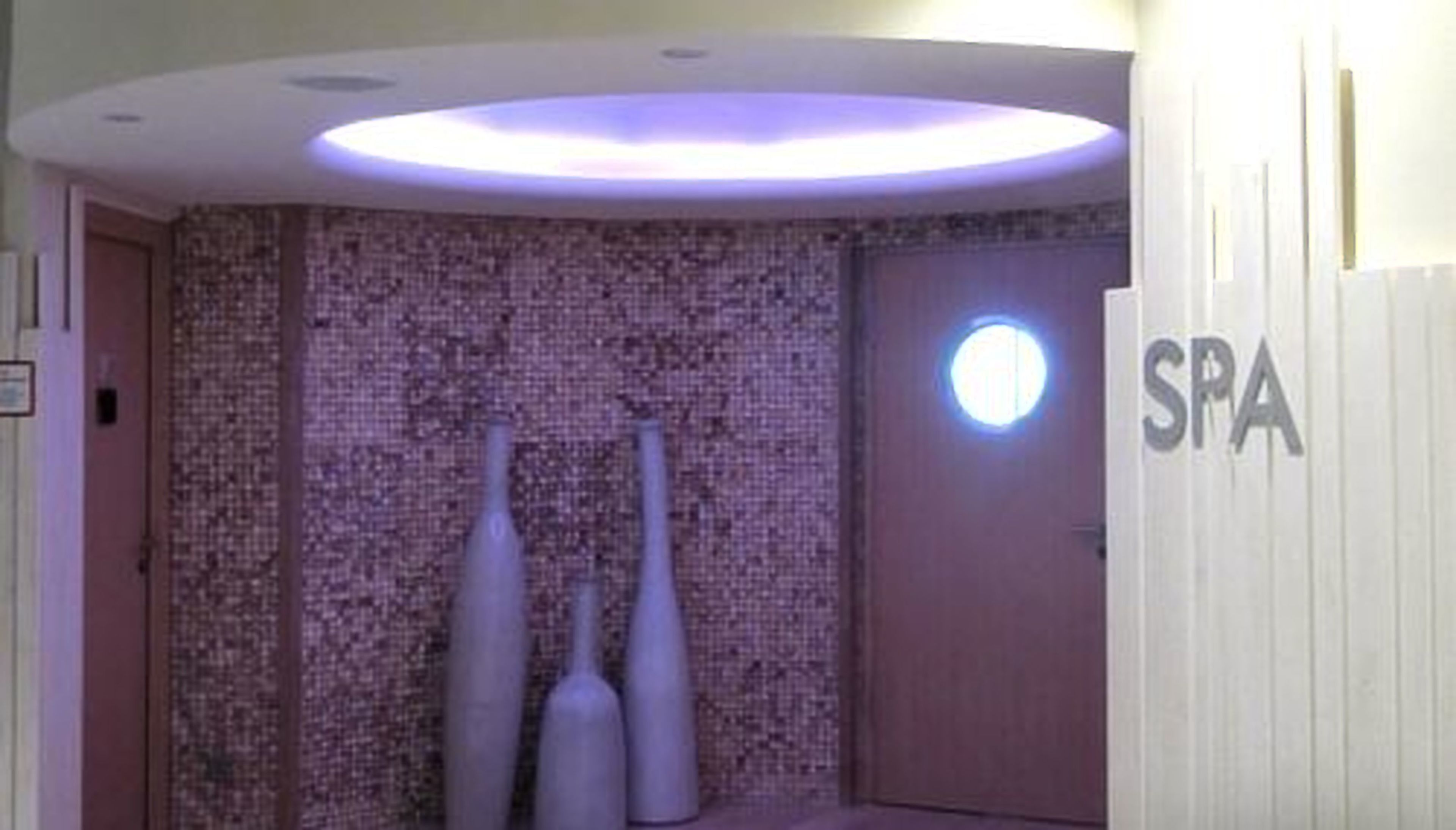 A spa area with a textured wall, three cylindrical vases, and a circular light fixture.