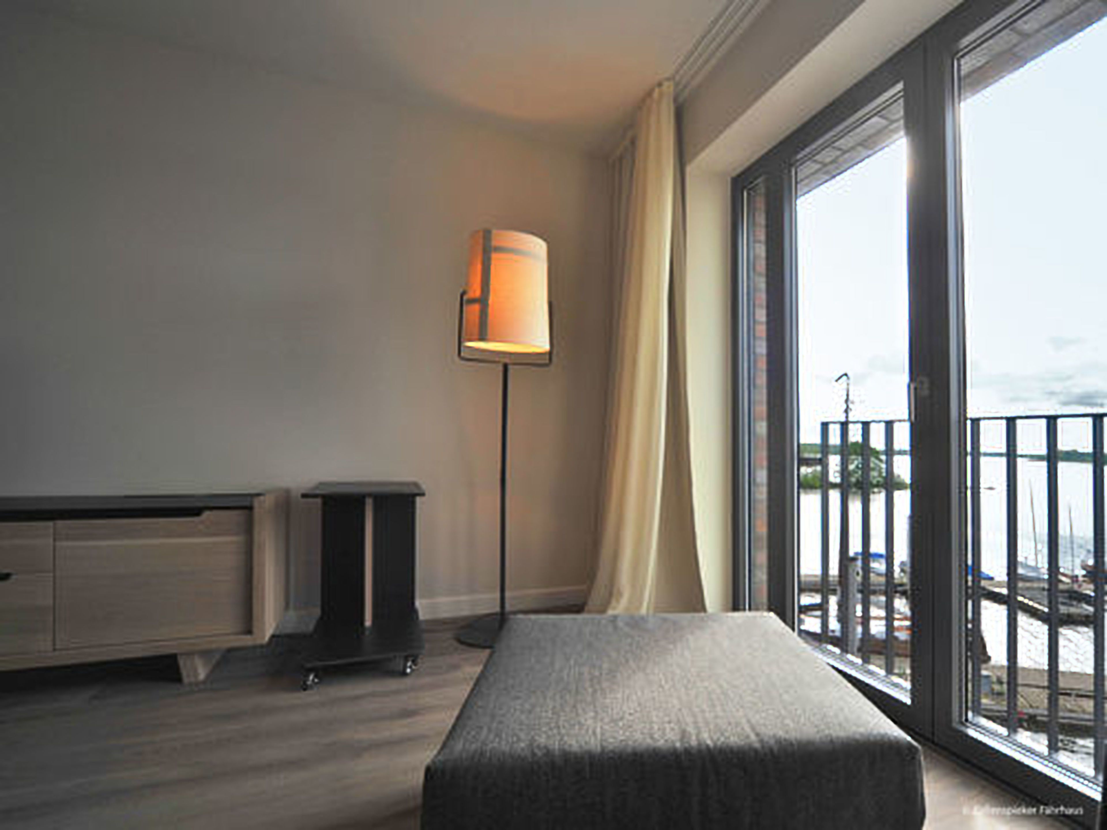A hotel room with a large window, a floor lamp, a bench, and a dresser.