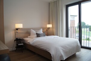 Ein Hotelzimmer mit einem großen Bett, zwei Nachttischlampen, einem Nachttisch und Blick durch ein großes Fenster nach draußen.