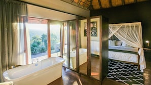 A bathroom with a bathtub, a shower, and a large window offering a view of the outdoors. - Tala Game Reserve (Camperdown)