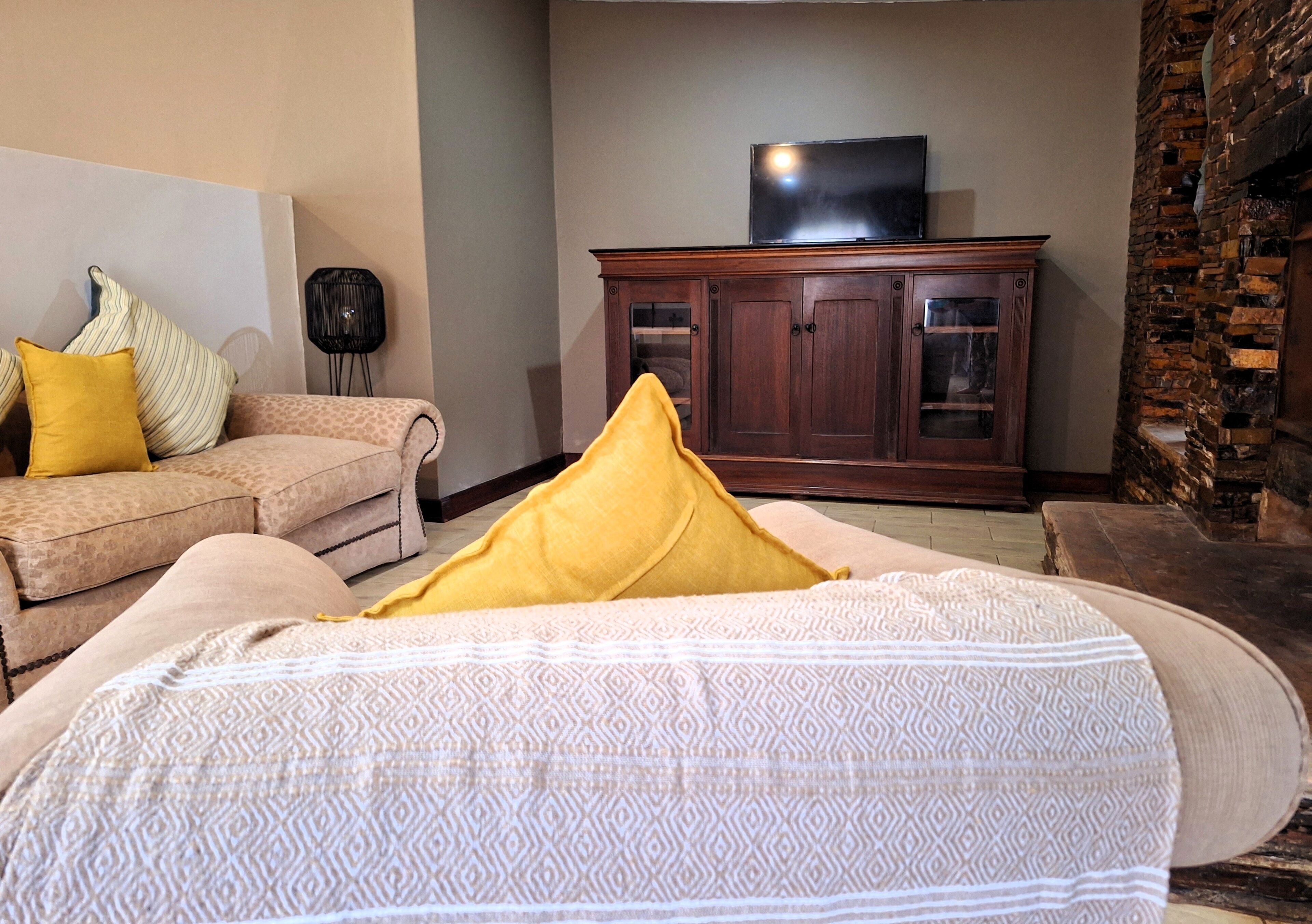 Una sala de estar con un sofá, un plaid estampado, un televisor sobre un mueble bajo y una chimenea de piedra.