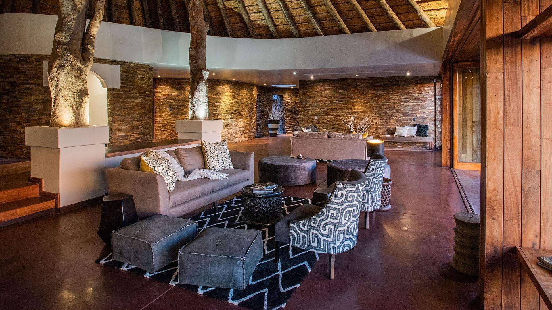A spacious lounge area with a stone wall, a high ceiling, and a seating arrangement including sofas and ottomans.