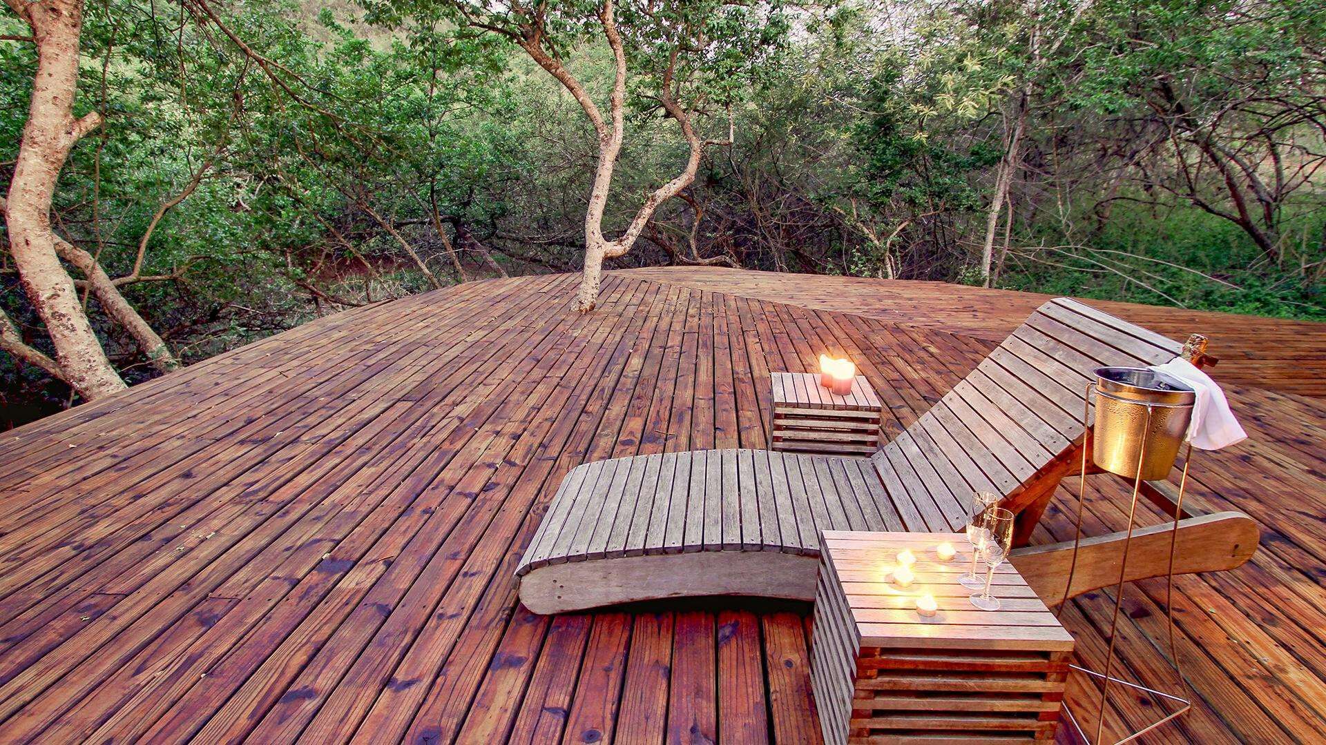 Une terrasse en bois avec des chaises longues et une table, entourée d’arbres.