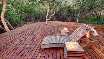 Une terrasse en bois avec des chaises longues et une table, entourée d’arbres.