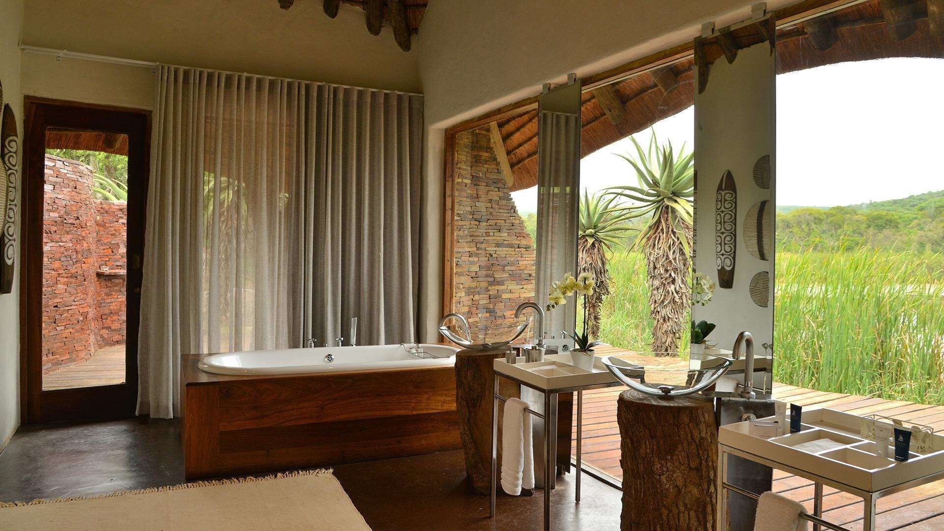 A bathroom with a bathtub, a sink, and a vanity. There is a view of greenery outside.
