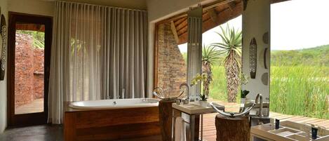 A bathroom with a bathtub, a sink, and a vanity. There is a view of greenery outside.
