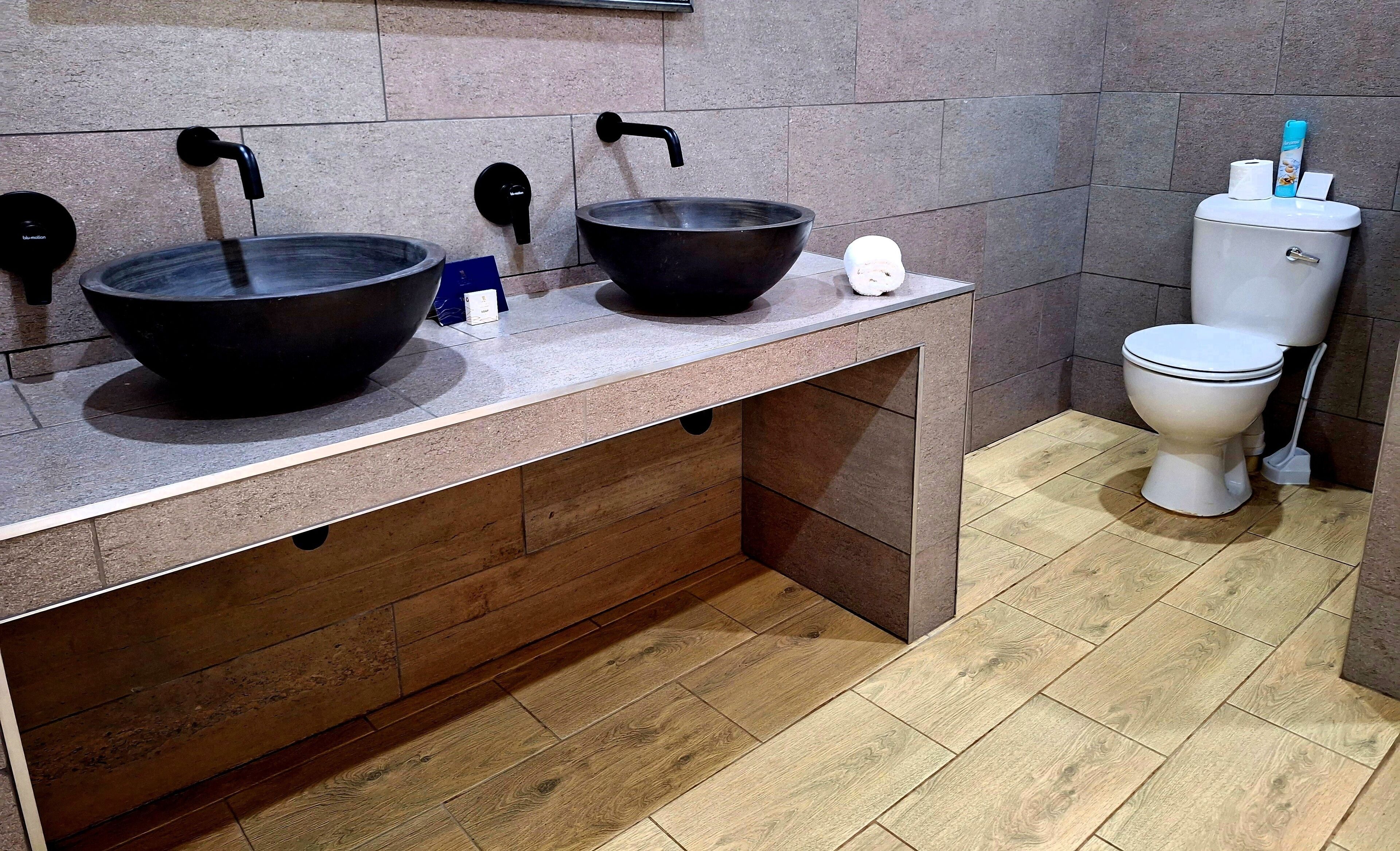A bathroom with two black sinks, a toilet, and a wooden vanity.