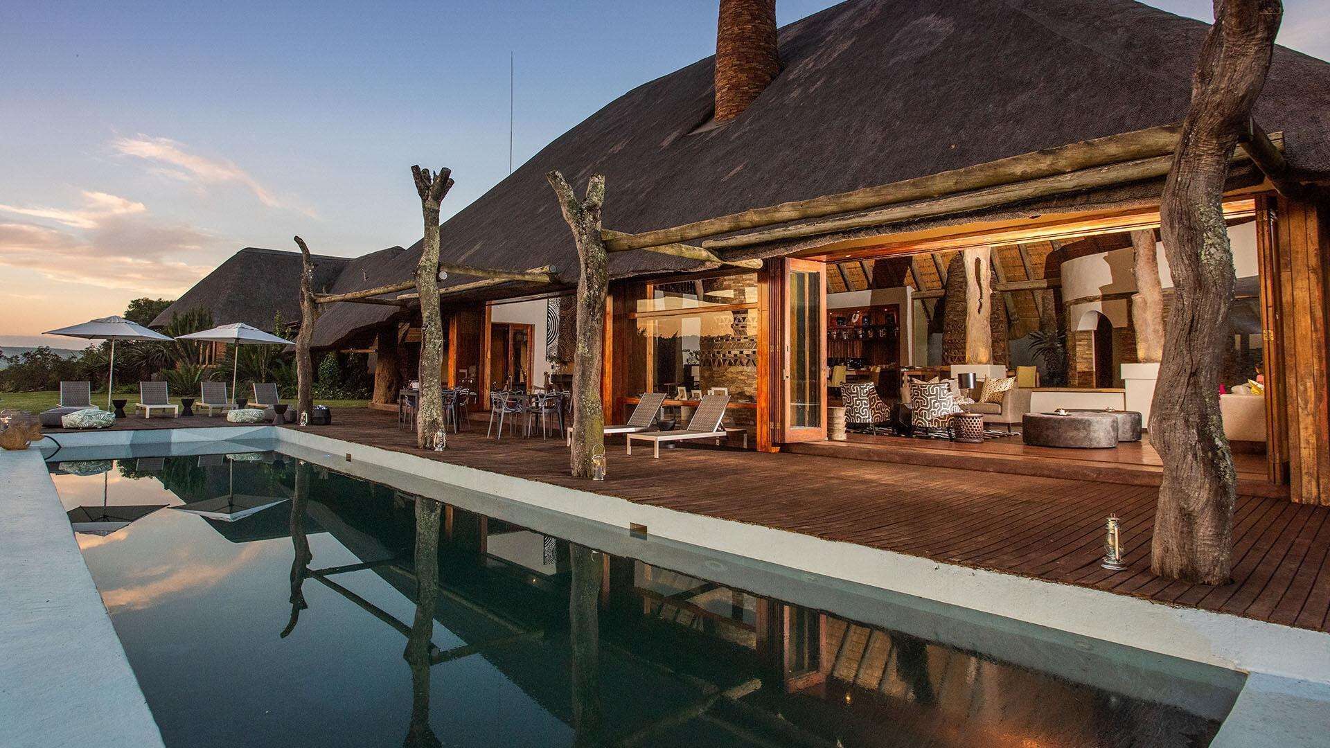 A resort with a pool, outdoor seating, and a thatched-roof building.