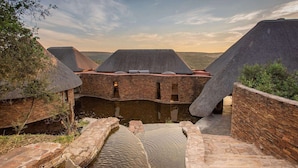 A traditional brick building with thatched roofs, a central water feature, and a view of the surrounding landscape. - Tala Game Reserve (Camperdown)