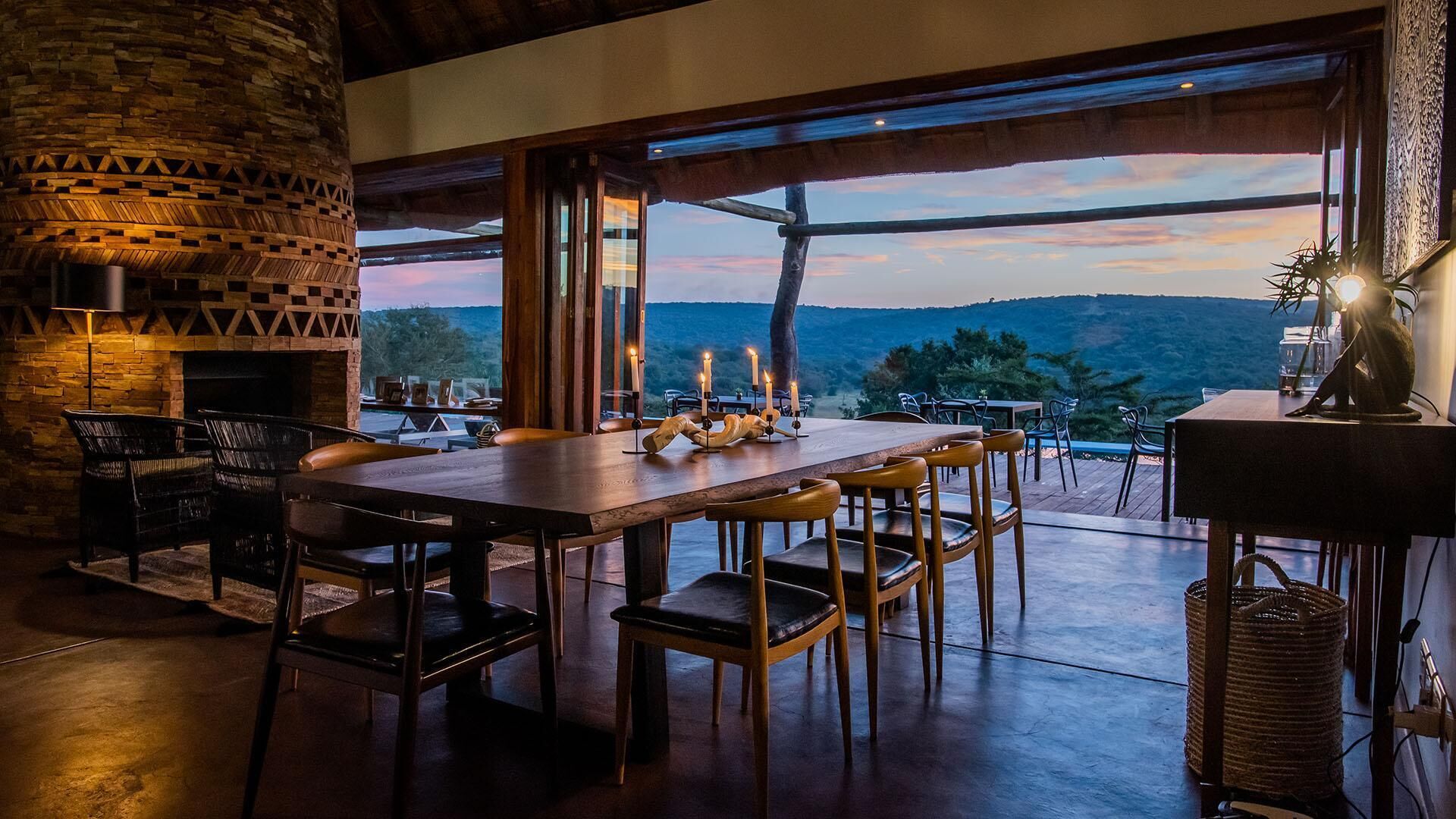 Un área de comedor al aire libre con chimenea de piedra, mesas y sillas de madera, con vistas a un paisaje pintoresco.
