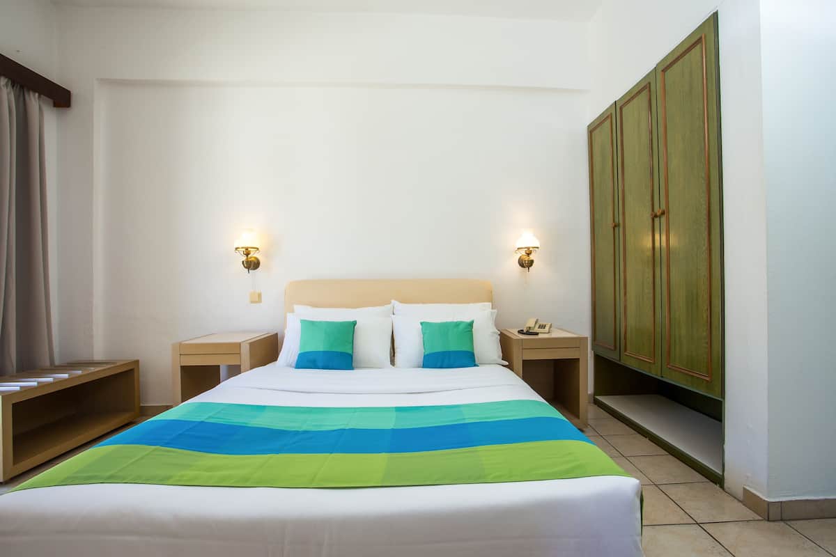 A neatly made bed with a striped blanket, two bedside tables with lamps, a wardrobe, and a window with curtains.