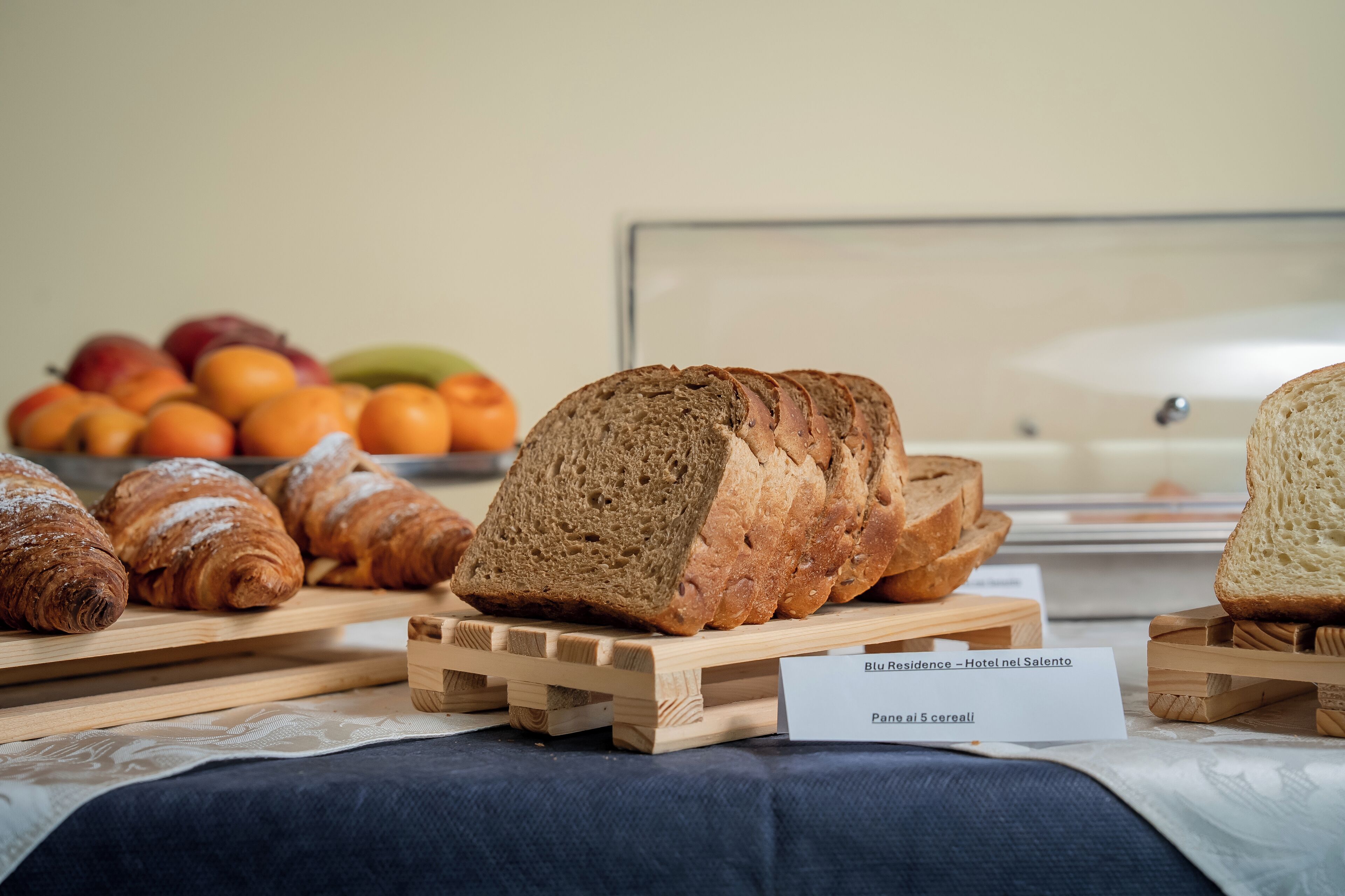 Diverse varietà di pane e pasticceria su supporti in legno, con un cartello che indica la posizione di un hotel.