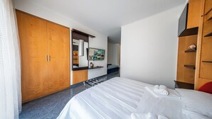 A hotel room with a large bed, wooden wardrobe, a mirror, and a small shelf with a vase. - Blu Residence (Casarano)