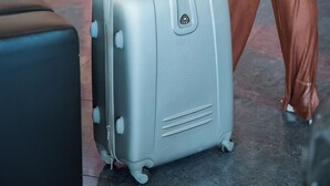 A person with a grey suitcase in a modern lobby with a red pillar and a black reception desk. - Blu Residence (Casarano)