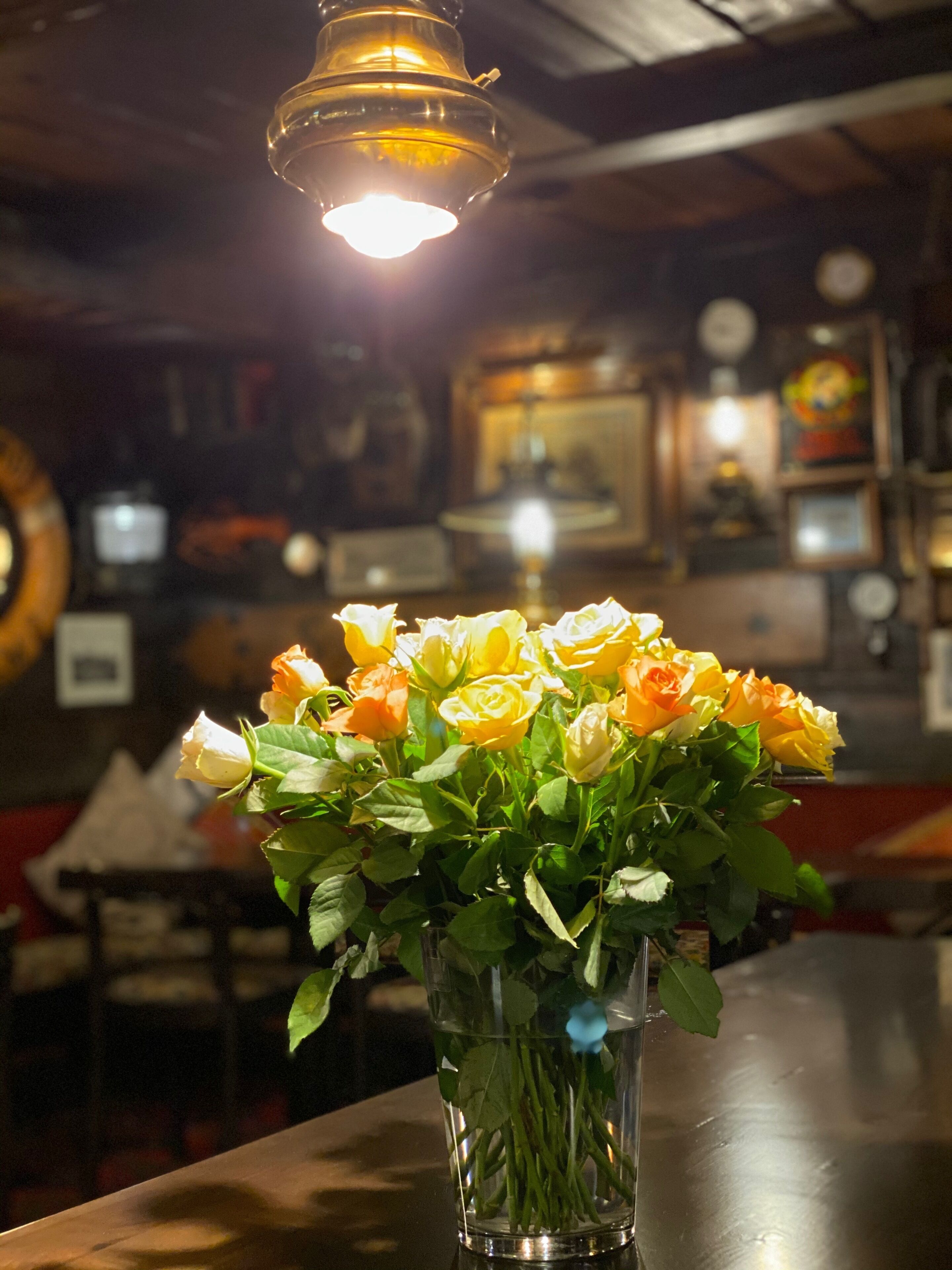 A vase with yellow and white roses on a table in a dimly lit room with a hanging light fixture.