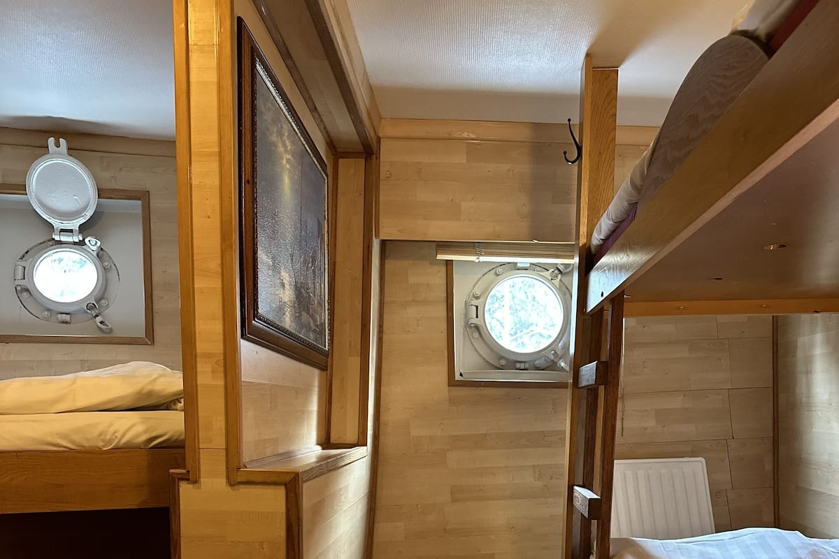 A compact, well-lit room with a bunk bed, a small window with a view, and a door leading to another area.