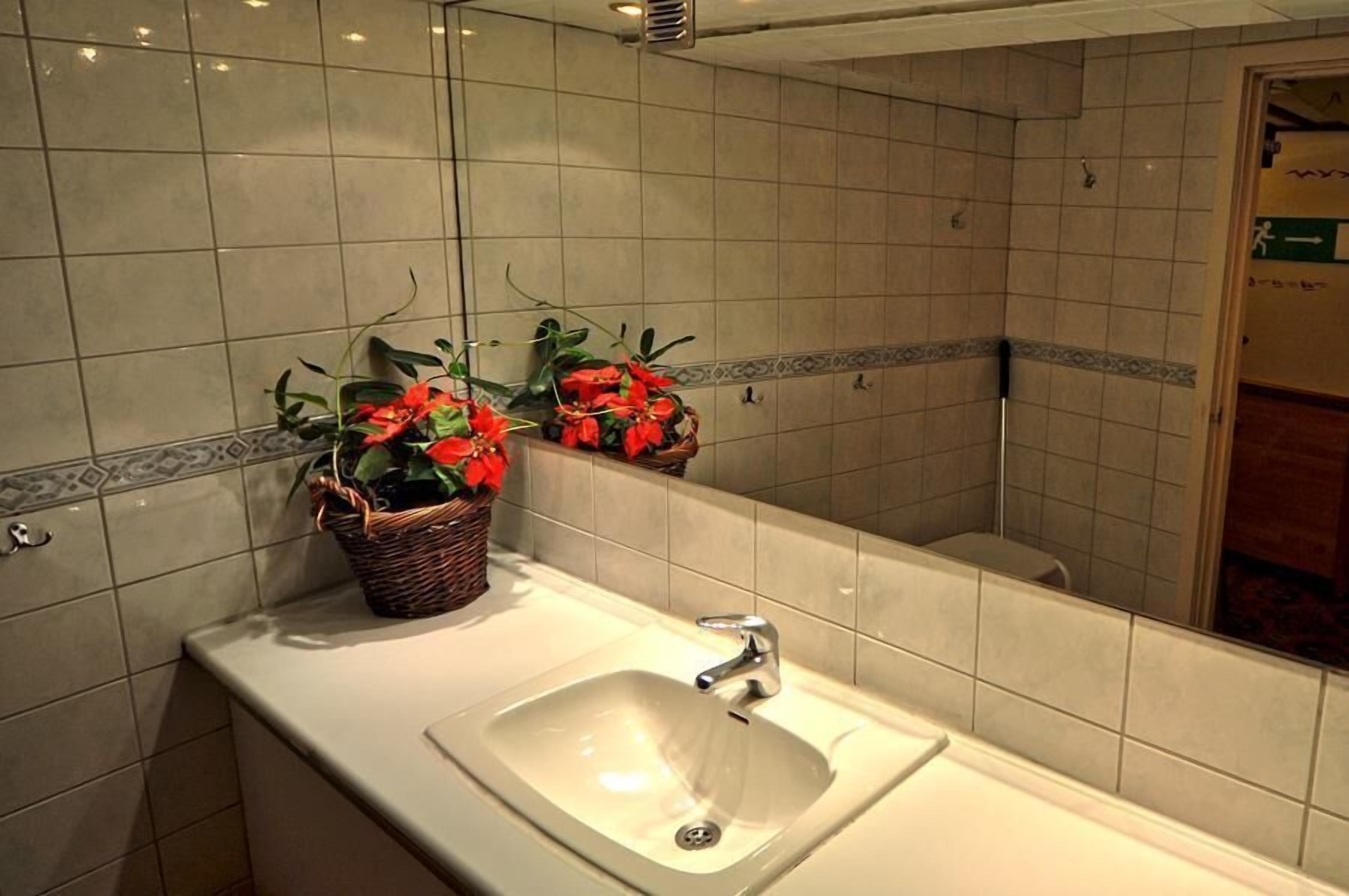 Une salle de bain avec un lavabo blanc, un miroir et deux paniers en osier ornés de fleurs rouges.