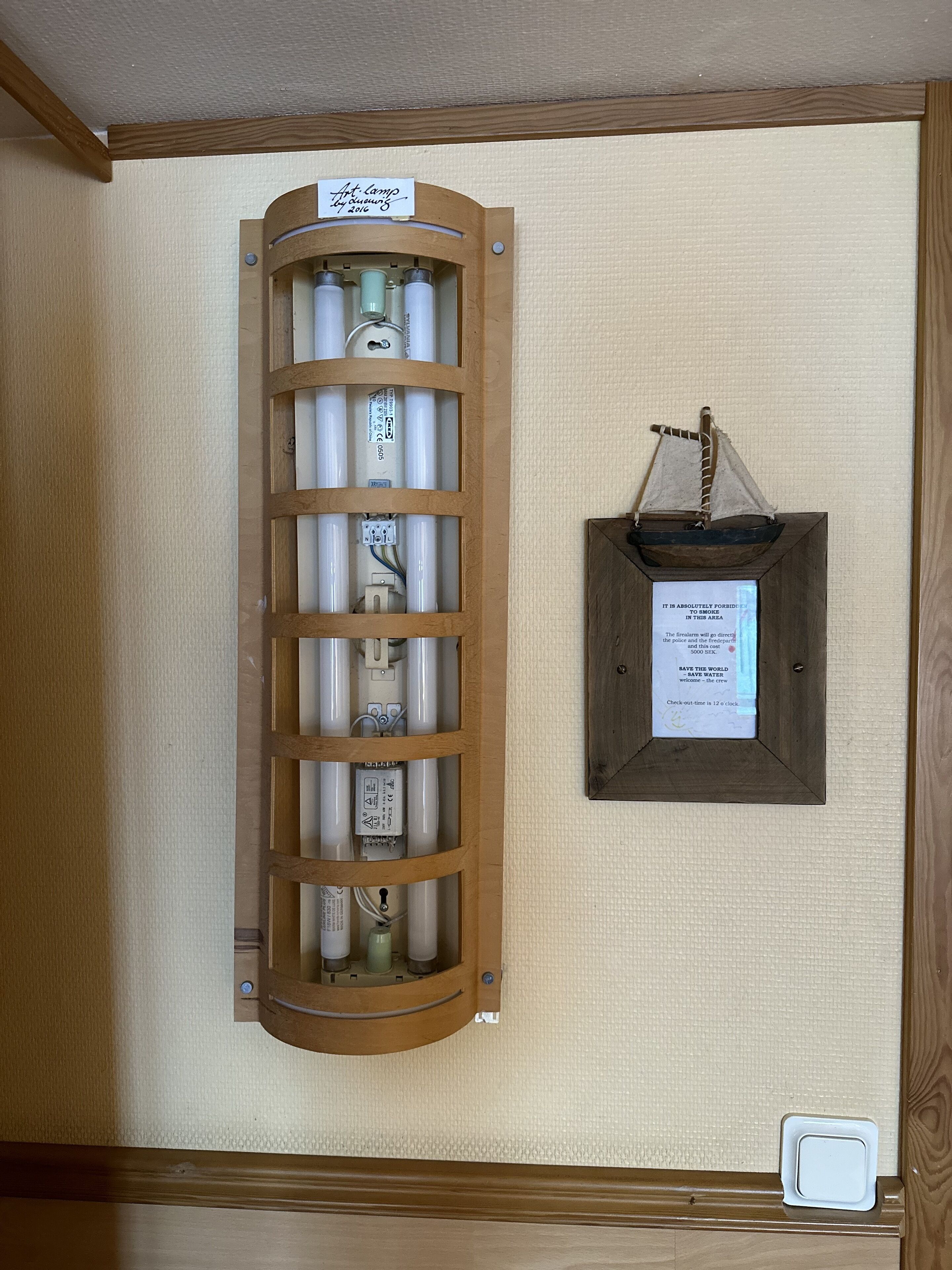 A wooden cabinet with a sign reading "Art. lamp by Lamping 2016" and a framed sign with a message about smoking.