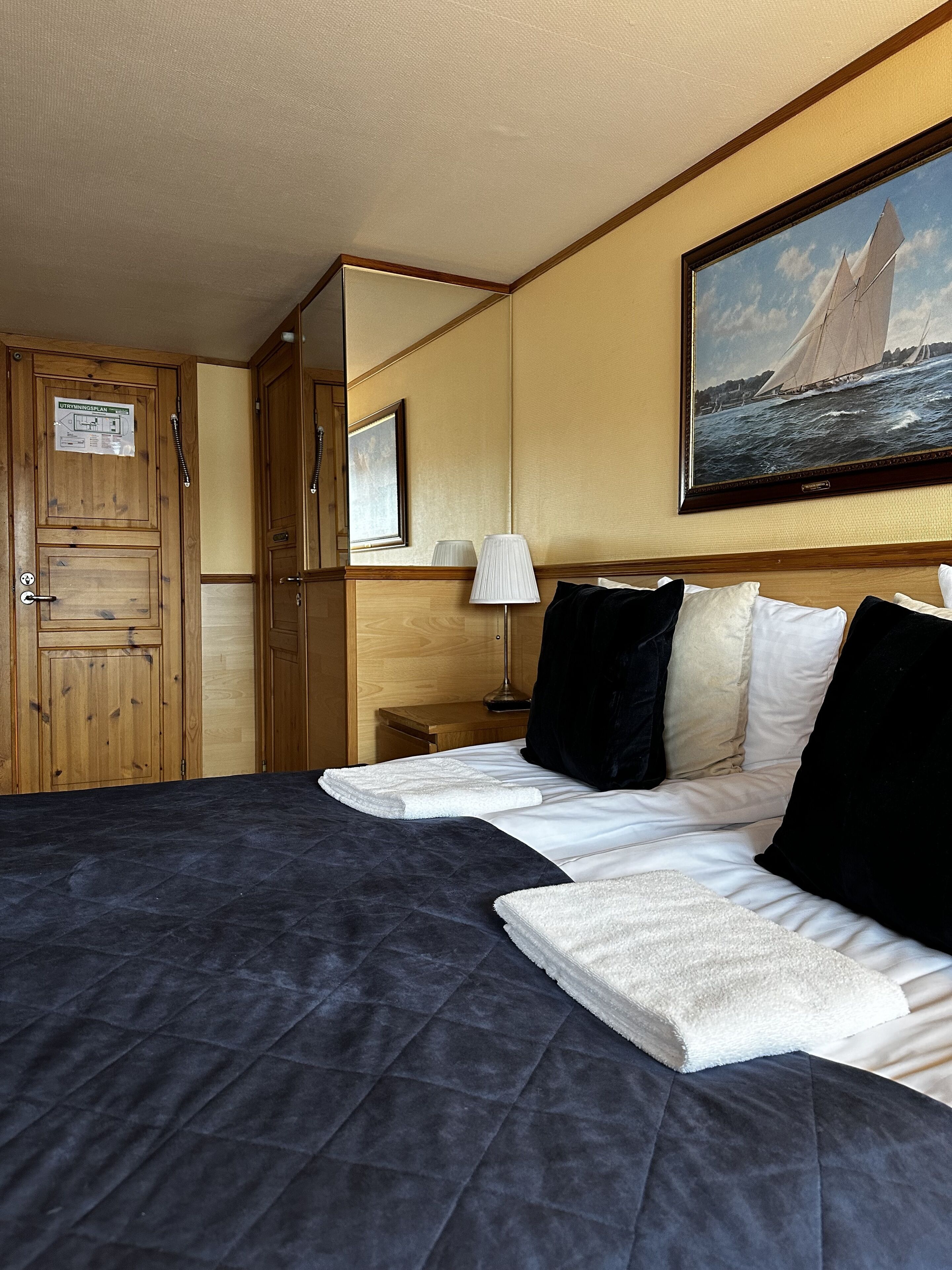 Una habitación de hotel con una cama grande, un cuadro de un velero, muebles de madera y un espejo.