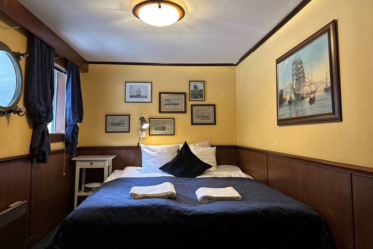 A hotel room with a bed, a nightstand, a lamp, and a painting on the wall.