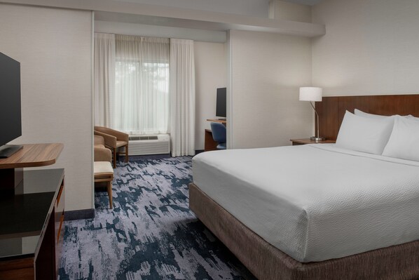 Habitación de hotel con una cama grande, un escritorio con computadora, una silla, un televisor y una ventana con cortinas.