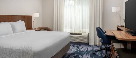 Habitación de hotel con una cama grande, un escritorio con una computadora, una silla y un televisor.